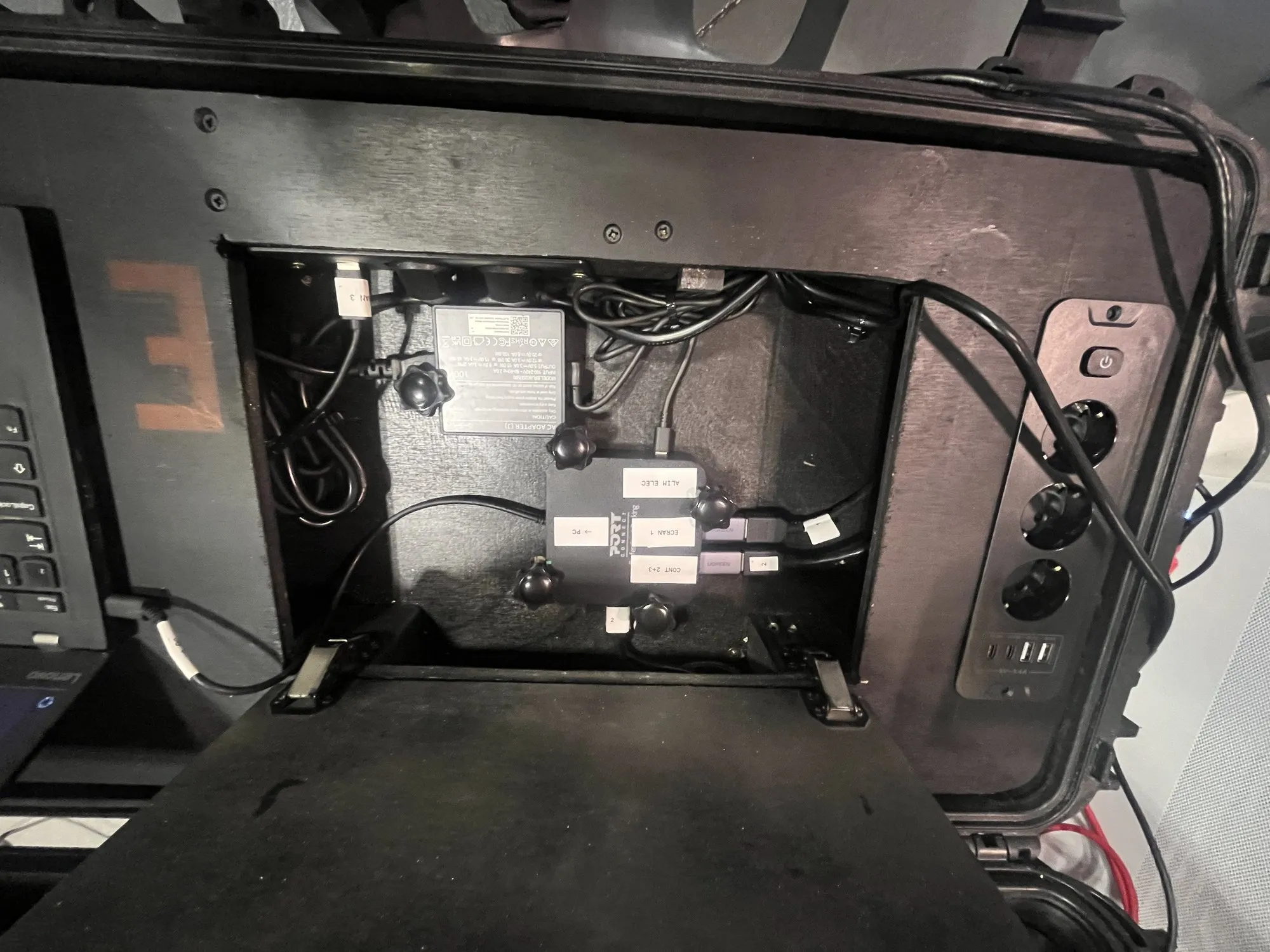 Trappe technique vue de dessus : blocs d'alimentation fixés et câblés, prises électriques et USB sur le flanc de la valise