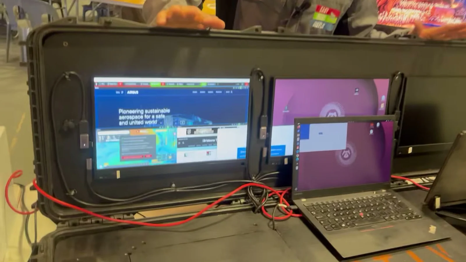 Der geöffnete Einsatzkoffer auf einem Vorführtisch: zwei eingeschaltete Bildschirme im Deckel, Steuer-Laptop und Kabel